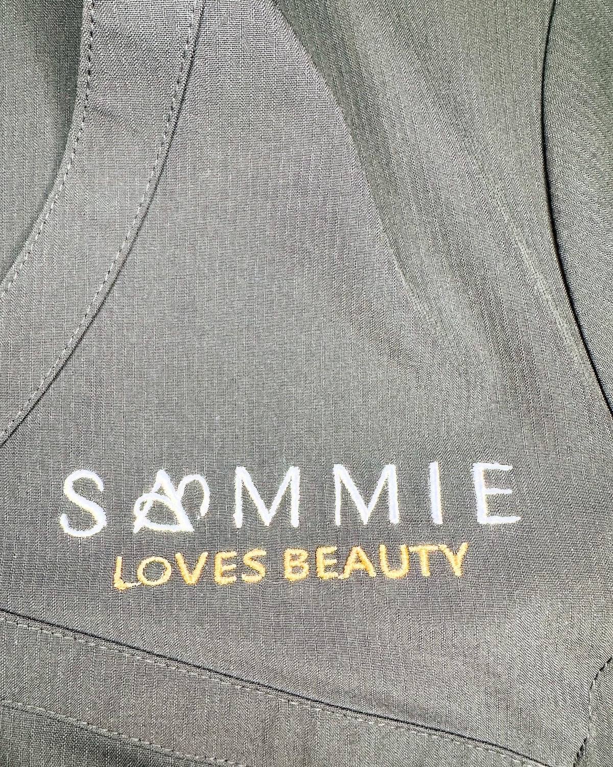 Close-up of the Sammie Loves Beauty logo embroidered on her tunic