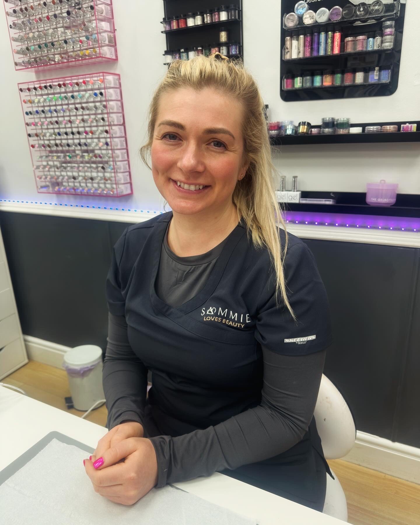 Sammie smiling at her nail desk, with racks of polish behind her